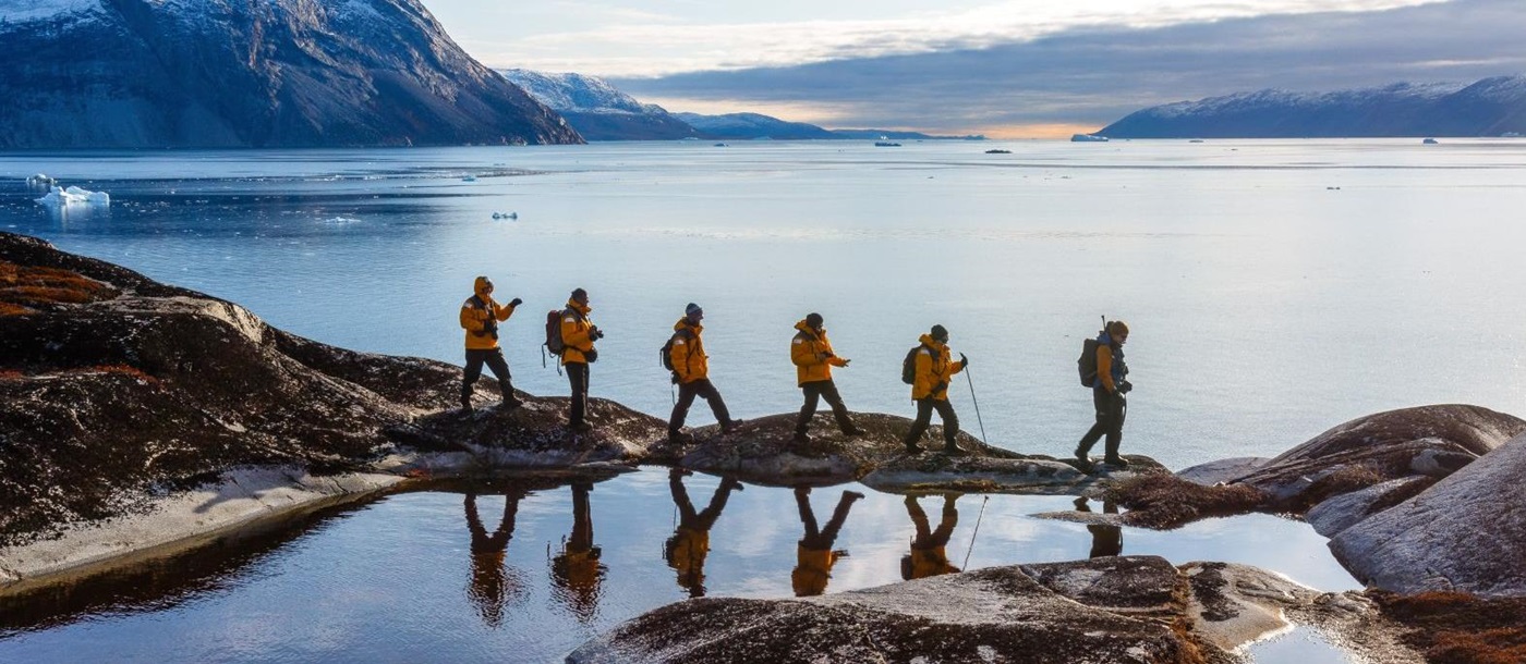 Hikers reflected in still Arctic fjord waters in Greenland
