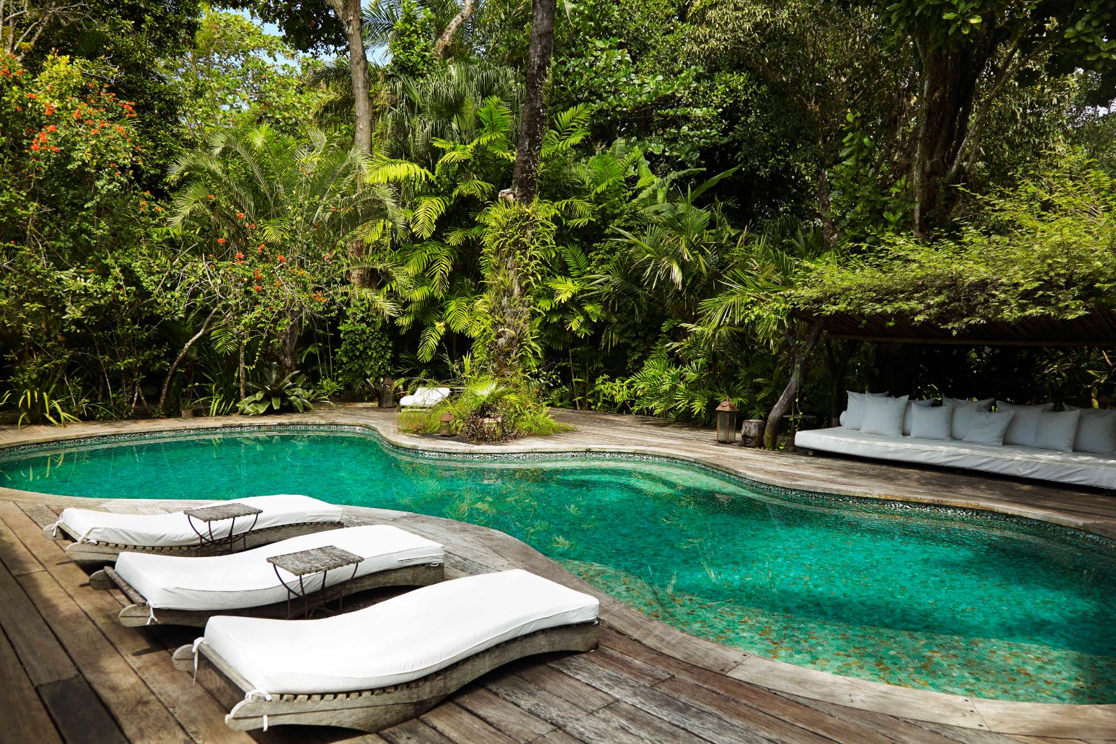 Serene outdoor pool with luxury sunbeds surrounded by tall trees and bushes at luxury resort Uxua Casa Hotel and Spa in Brazil