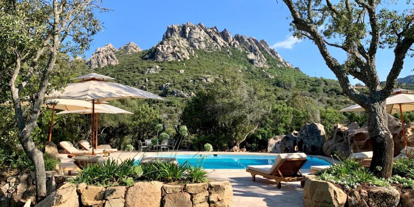 Pool terrace with rockery, sun loungers, parasols and mountain view at Villa Pantaleo on Sardinia, Italy
