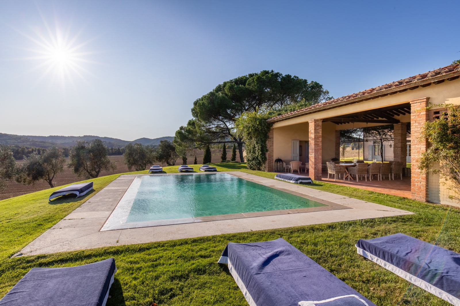 Pool area with sun loungers and covered outdoor dining area in garden at La Vigna in Tuscany, Italy