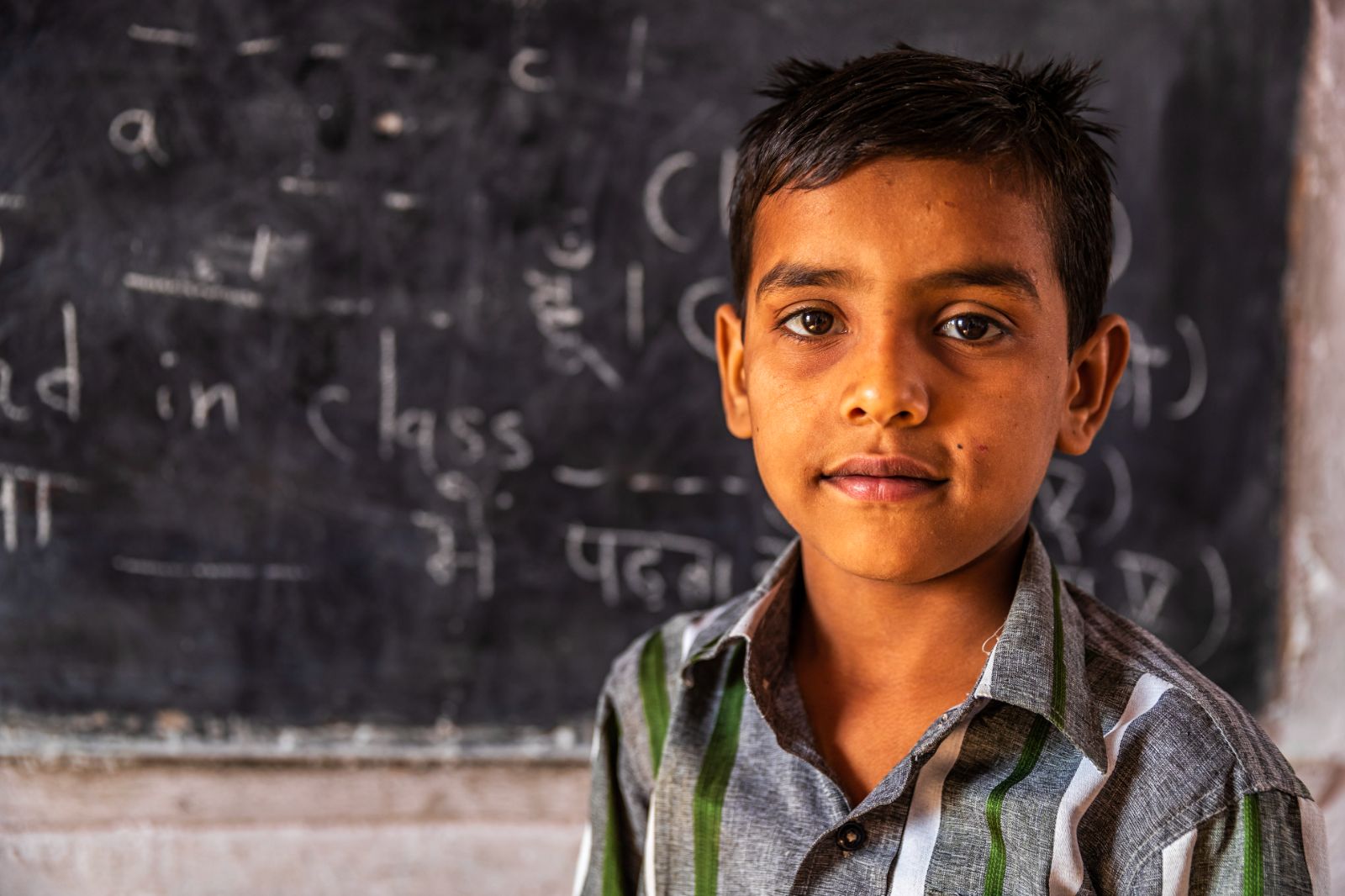 Young boy standing in front of a blackboard at school in India