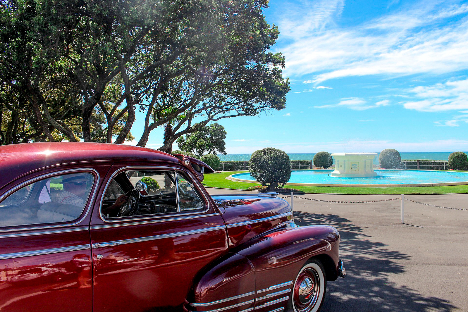A retro car parked by an Art Deco fountain overlooking the ocean in Napier, New Zealand