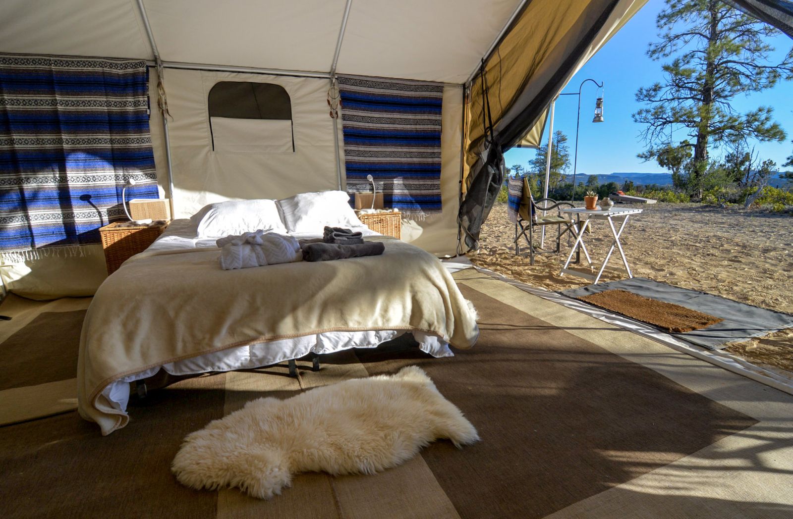 King bed in a tent at a private camp in Yellowstone National Park with outdoor table and views over the park