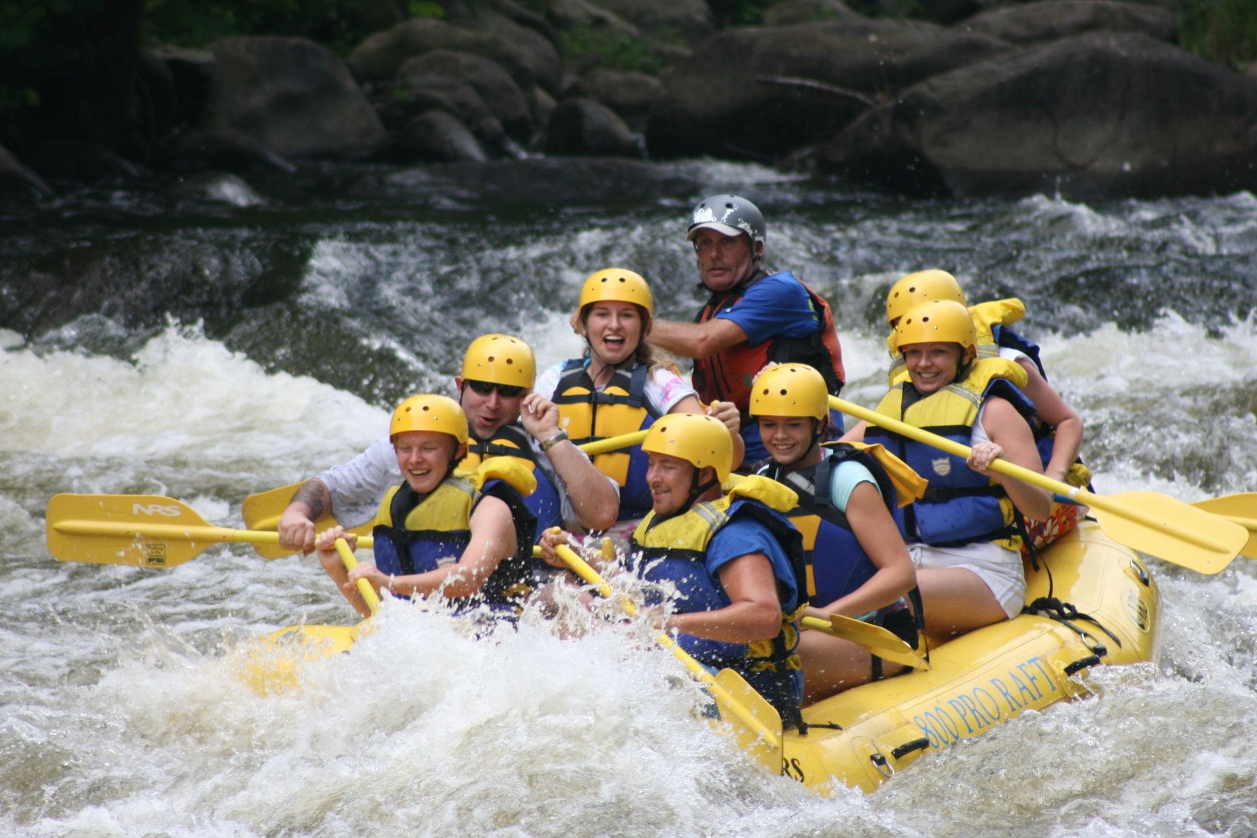 Group of people white water rafting through river rapids