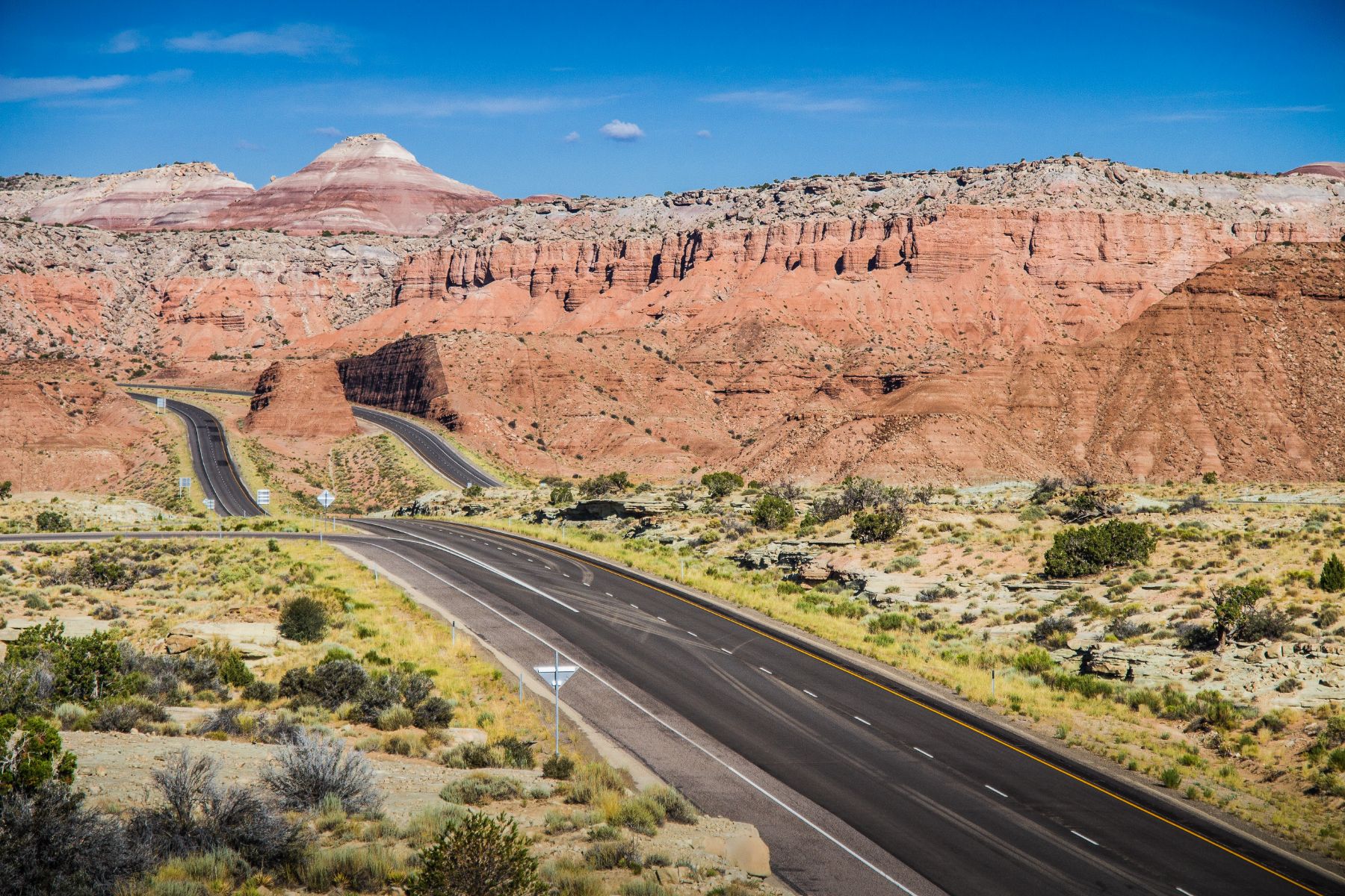 An empty road alongside red sandstone cliffs in southwest USA