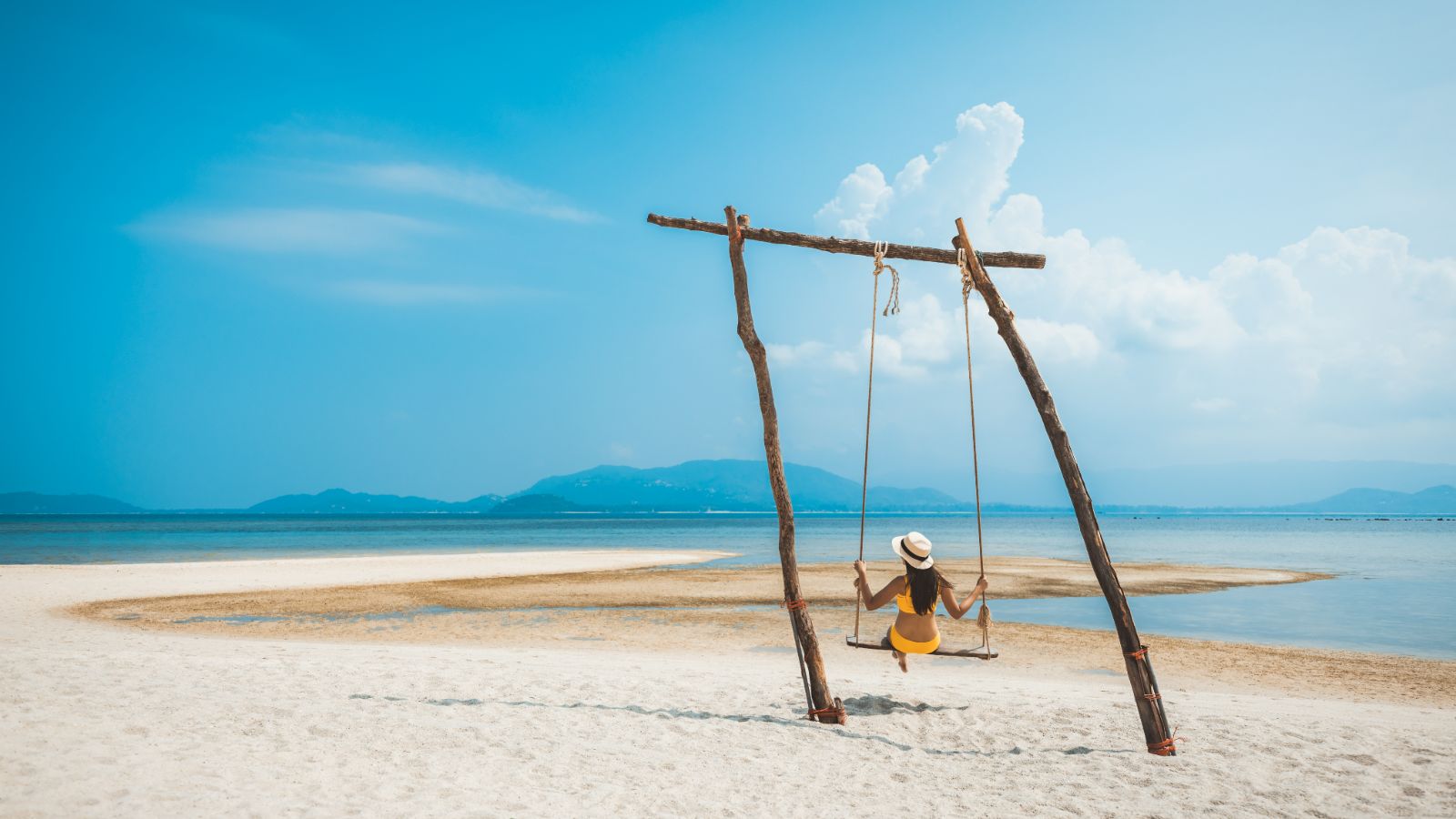 Lady on a swing on a deserted white sand beach in Asia